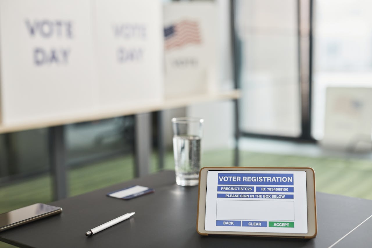 Tablet displaying digital voter registration at indoor voting station with vote day signs.